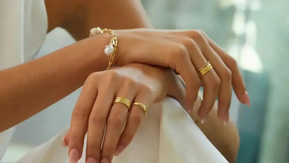 Elegant hands showcasing gold silver platinum jewelry with rings and a bracelet.