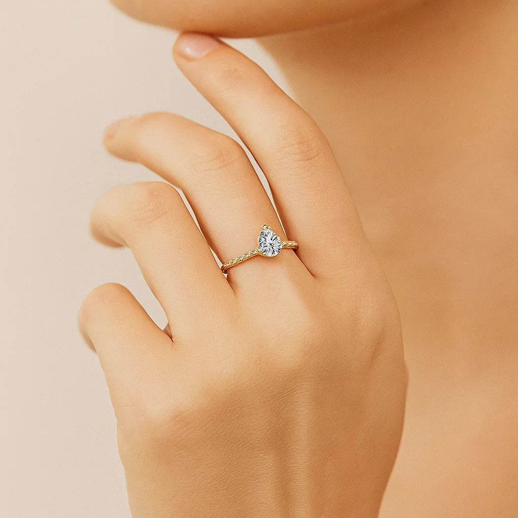 Gold Plated ring with a Pear-shaped diamond on a hand against a beige background