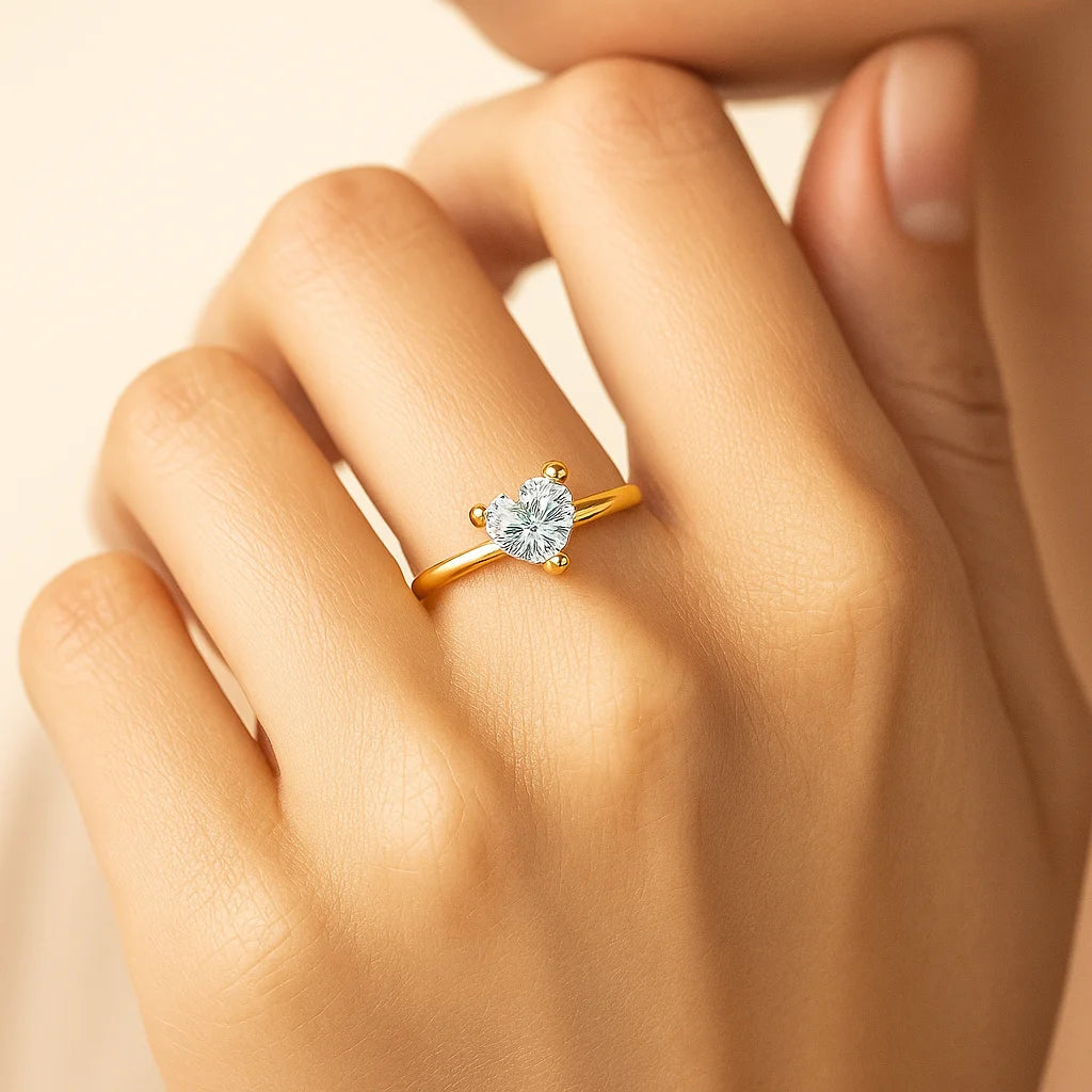 Gold Plated ring with a heart-shaped diamond on a hand against a beige background