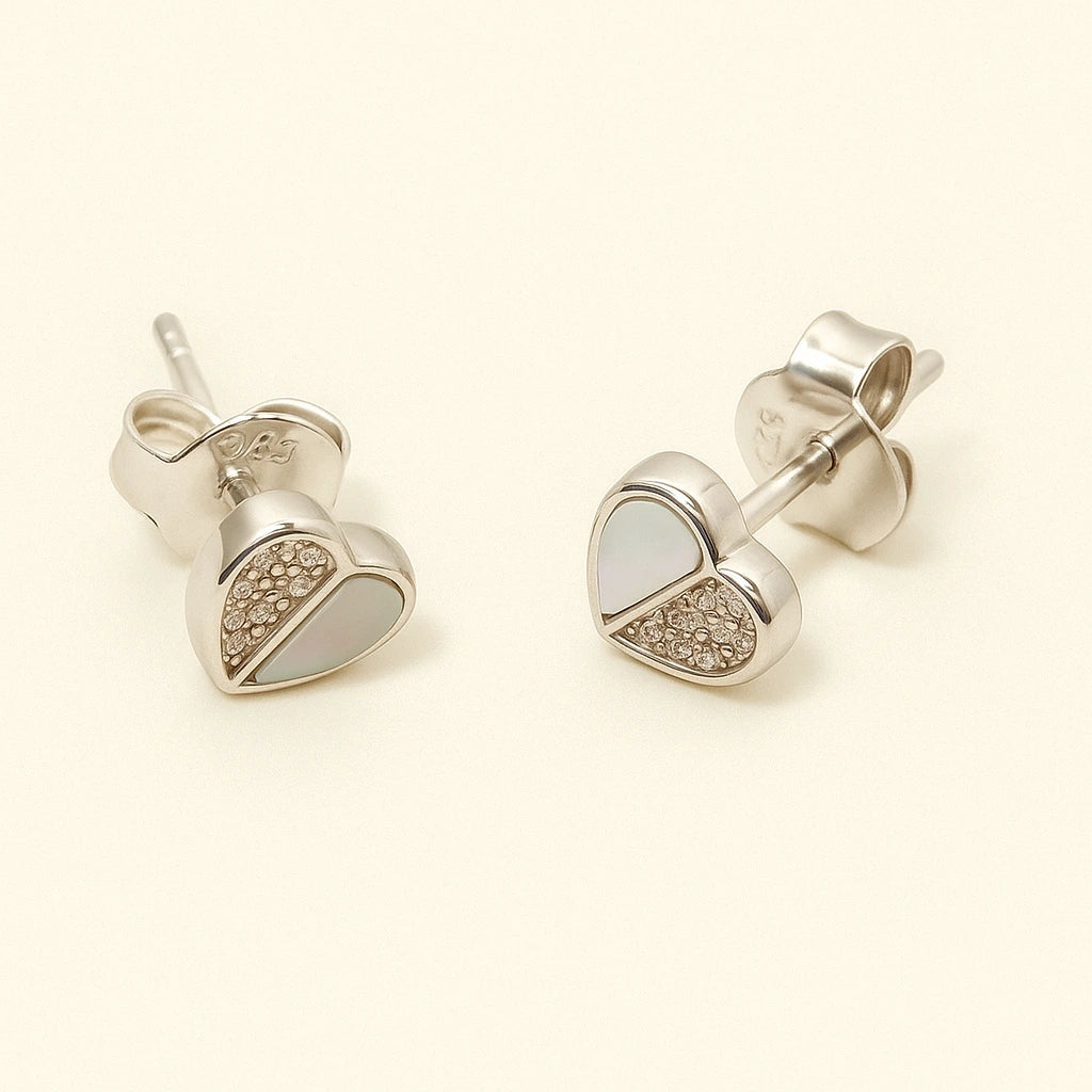 Heart-shaped silver earrings with gemstones on a beige background
