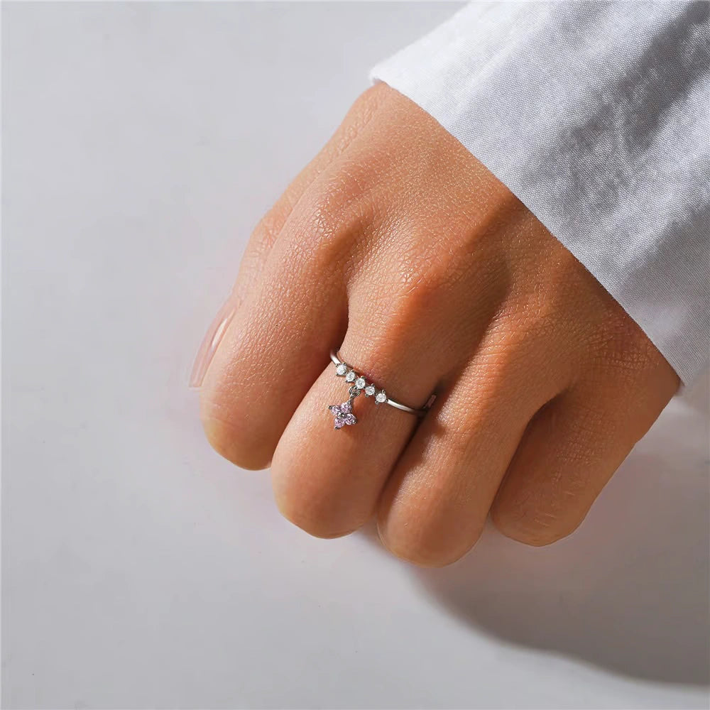 Hand wearing a ring with a star-shaped gem on a light gray background