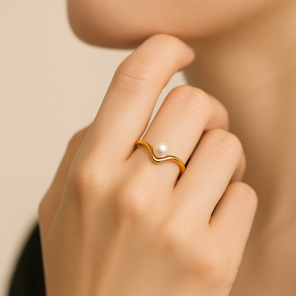 Gold ring with a pearl on a hand against a beige background