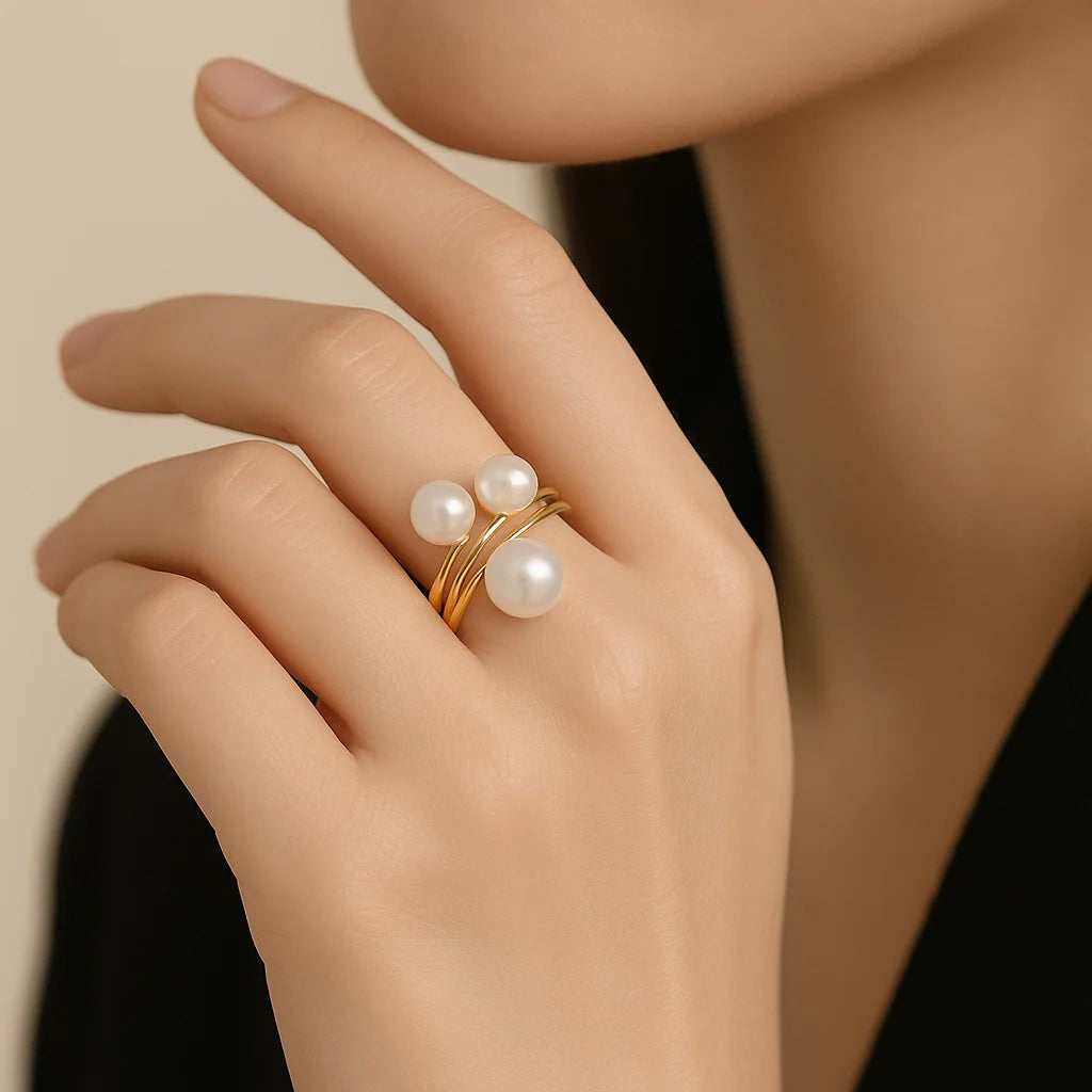 Hand wearing a golden ring with pearls against a neutral background