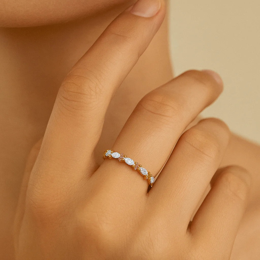 Close-up of a hand wearing a delicate ring with small stones on a neutral background
