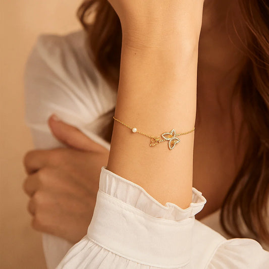 Gold bracelet with a starfish charm on a person's wrist against a neutral background