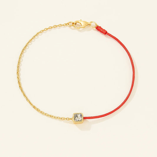 Bracelet with red cord and gold clasp on a beige background