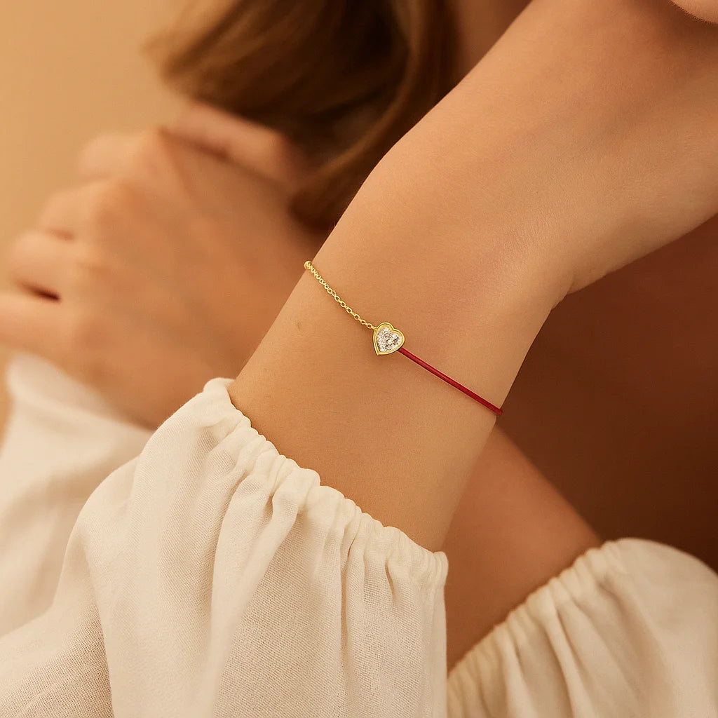 Close-up of a wrist wearing a delicate gold bracelet with a heart-shaped gemstone on a beige background.