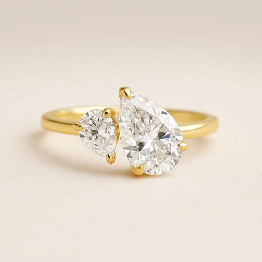 Gold ring with two pear-shaped diamonds on a beige background