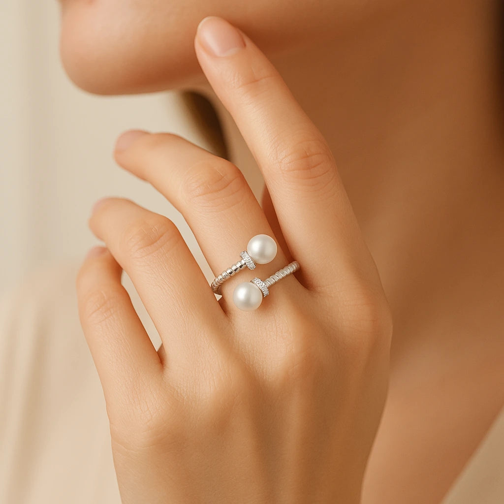 Close-up of a hand wearing two pearl rings on a neutral background