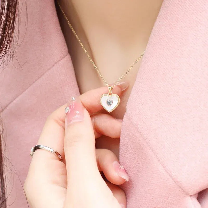Heart-shaped pendant necklace being held by a person wearing a pink coat.