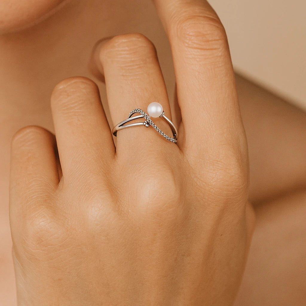 Silver ring with a pearl on a person's finger against a neutral background